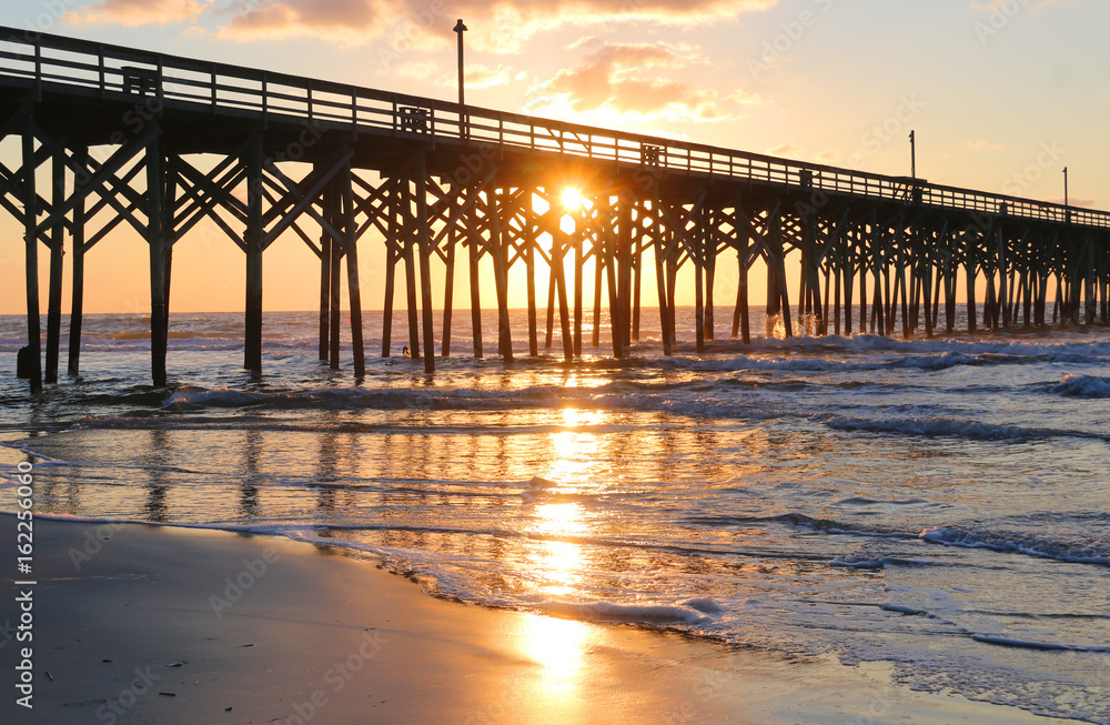 Sunrise at a South Carolina Atlantic coast, Myrtle Beach area, USA. Landscape with the reflection of the sun in shallow water on the foreground and a wooden pier on the background.Vacation background.
