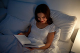young woman reading book in bed at night home