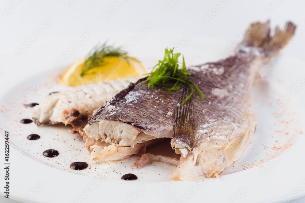 grilled dorada in salt with lemon slice on a white plate on a light background (close)