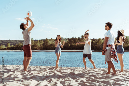 young multiethnic friends playing volleyball on sandy beach at daytime