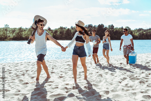 group of happy friends walking on beach on summer day