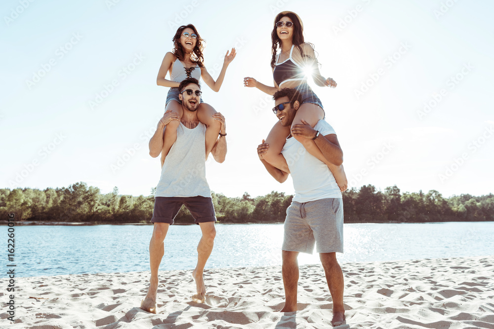 happy friends piggybacking and enjoying summertime while spending time on beach happy friends piggybacking and enjoying summertime while spending time on beach