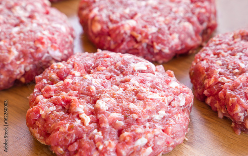 Organic raw ground beef, round patties for making homemade burger on wooden cutting board