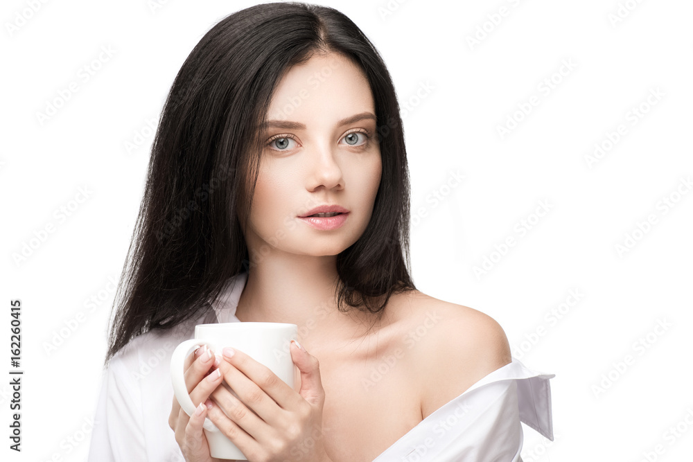 Gorgeous young woman holding cup with hot beverage and looking at camera Gorgeous young woman holding cup with hot beverage and looking at camera