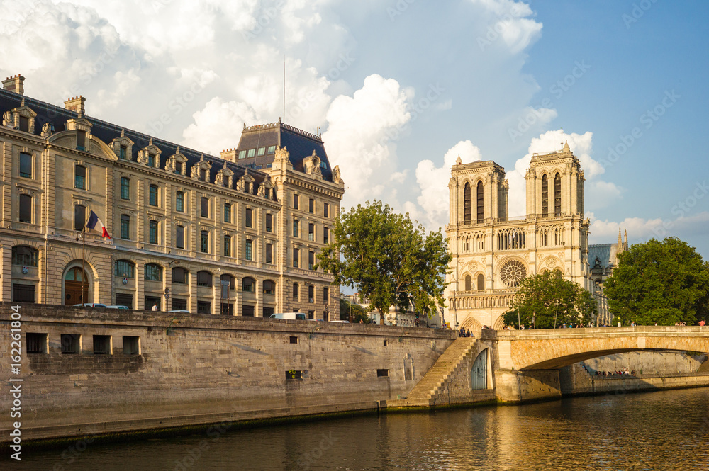 Notre-Dame cathedral in Paris and the Police headquarters under a warm sunlight with the river Seine in the foreground.