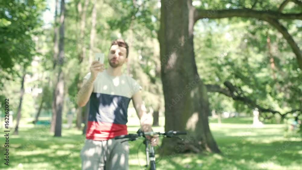 Handsome man having a videochat on smartphone while walking with bicycle in the park, steadycam shot
Handsome man having a videochat on smartphone while walking with bicycle in the park, steadycam shot