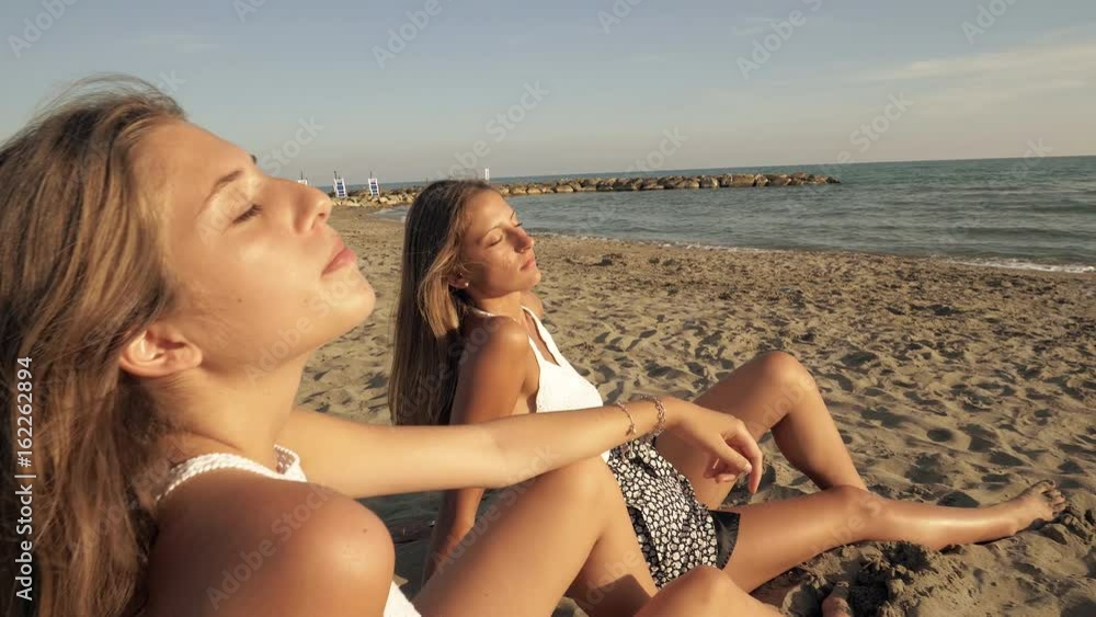 Dolly shot from closeup to medium shot on beach of two girls sun bathing at sunset happy Dolly shot from closeup to medium shot on beach of two girls sun bathing at sunset happy