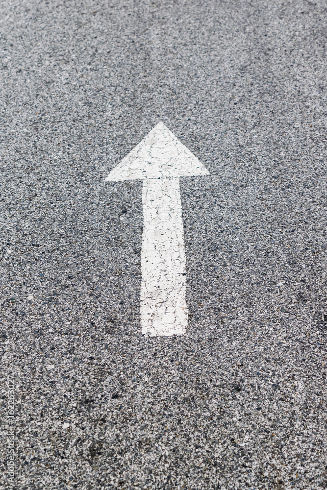 White arrow on cracked asphalt surface. Concept traffic. White arrow on cracked asphalt surface. Concept traffic.