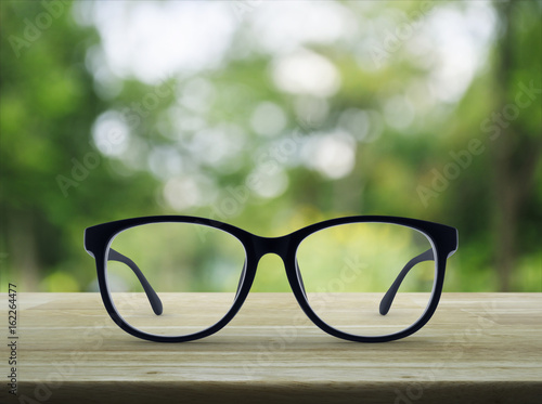 Black eye glasses on wooden table over blur green tree background, Business vision concept