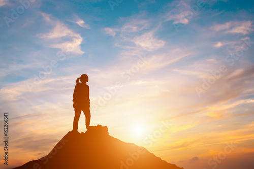Silhouette of woman standing on hill in sunset.