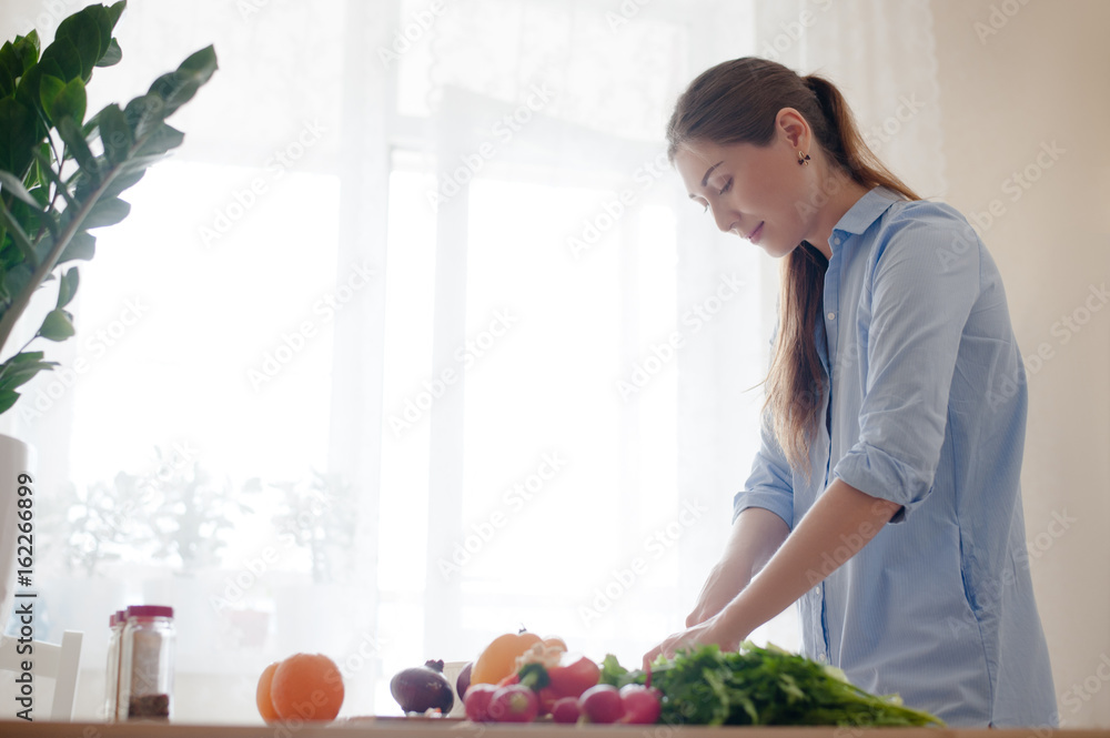 Beautiful girl-a vegetarian standing in the bright kitchen and prepares a lunch of fresh vegetables