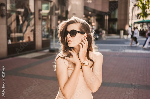 Close-up portrait of a slender young girl blogger beautiful brunette in downtown dusseldorf in a pastel dress and a lady wearing sunglasses walking poses and smiling on the sunset