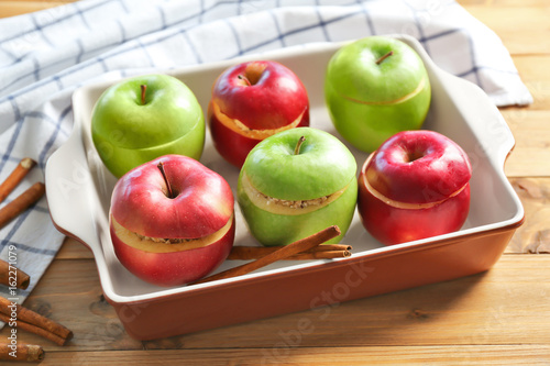 Fresh stuffed apples with cinnamon in baking dish on wooden table photo