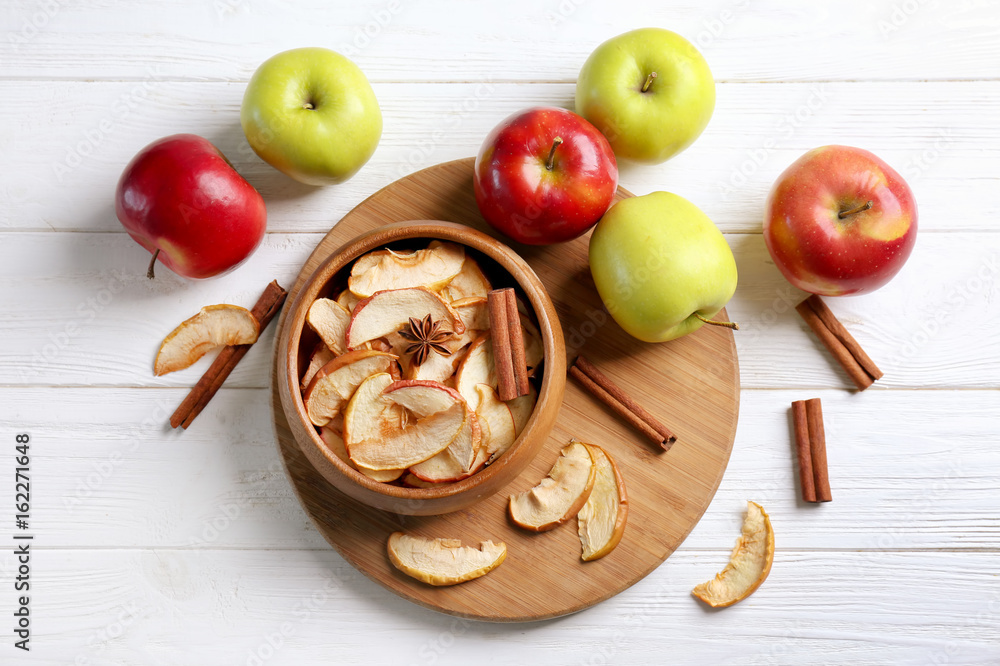Composition with tasty apple chips and cinnamon on light wooden table Composition with tasty apple chips and cinnamon on light wooden table