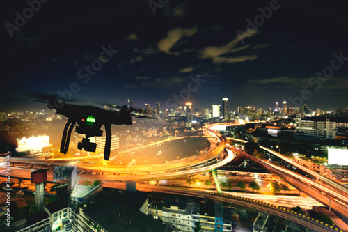  Drone (Multi-rotor) silhouette flying above the city panorama at night scene.