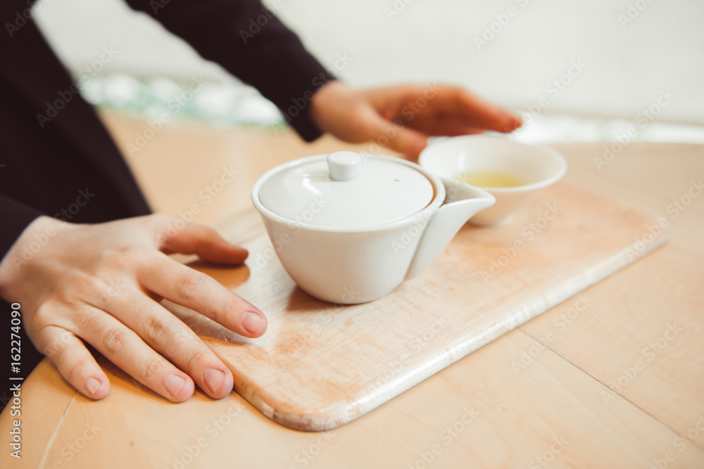 Hands holding Japanese Sencha Tea in clay pot.
