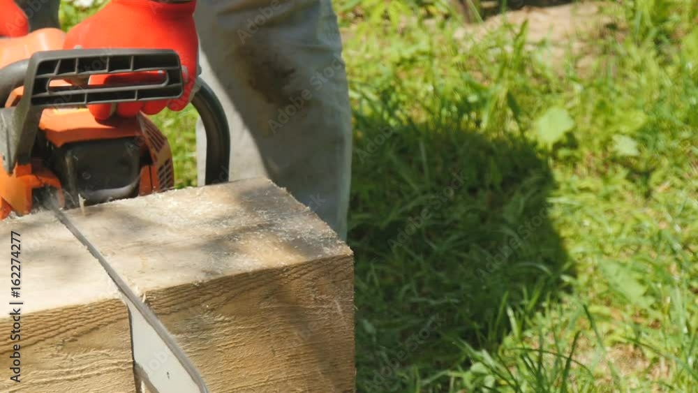 A worker cuts a wooden beam with a gasoline saw A worker cuts a wooden beam with a gasoline saw