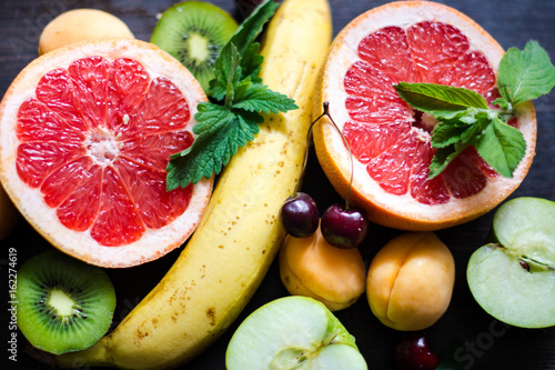 спелые, сочные фрукты и ягоды: яркий красный сочный грейпфрут, зеленый киви, желтый банан, черешня, мята, абрикос и зеленое яблоко