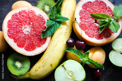 спелые, сочные фрукты и ягоды: яркий красный сочный грейпфрут, зеленый киви, желтый банан, черешня, мята, абрикос и зеленое яблоко