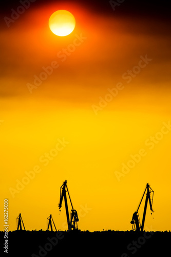 Landscape of a cranes in a harbor at sunset with clouds