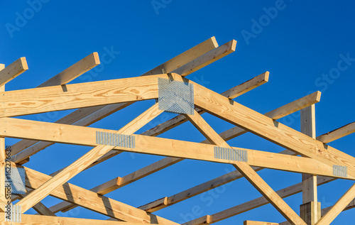 A new build roof with a wooden truss framework with a blue sky background.