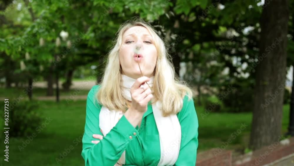 A woman is blowing a dandelion. Girl with dandelion in the park. A woman is blowing a dandelion. Girl with dandelion in the park.