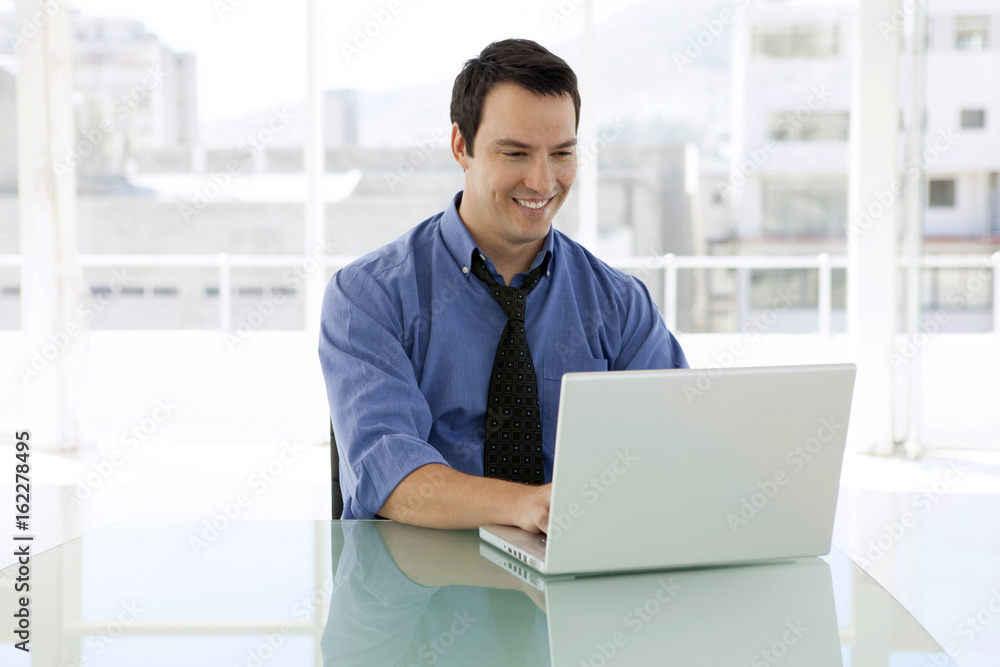 Young smiling businessman with blue shirt working on laptop at business startup workplace Young smiling businessman with blue shirt working on laptop at business startup workplace