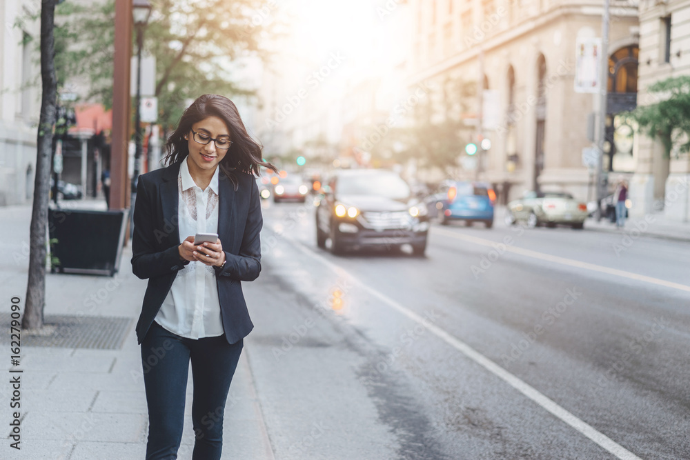 Successful female banker working outdoor via smartphone while walking near her office