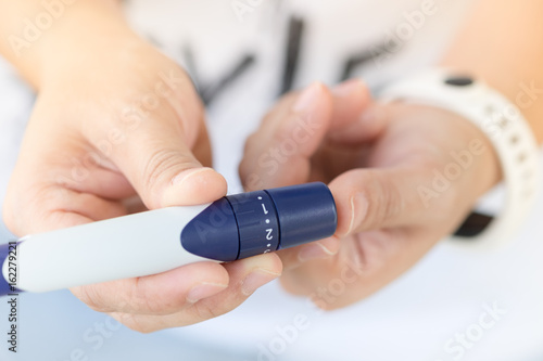 Close up of woman hands using lancet on finger to check blood sugar level by Glucose meter using as Medicine  diabetes  glycemia  health care and people concept.