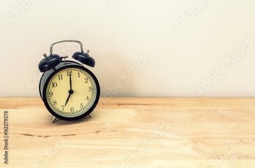 Wallpaper Mural retro black color alarm clock times at 7 o'clock morning on wooden table table and white wall, vintage tone Torontodigital.ca