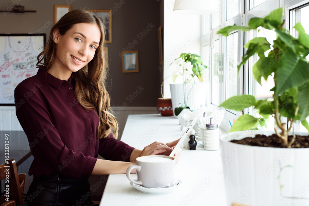 Concentrated at work. Confident young woman in smart casual wear working on laptop while sitting near window in creative office or cafe Concentrated at work. Confident young woman in smart casual wear working on laptop while sitting near window in creative office or cafe