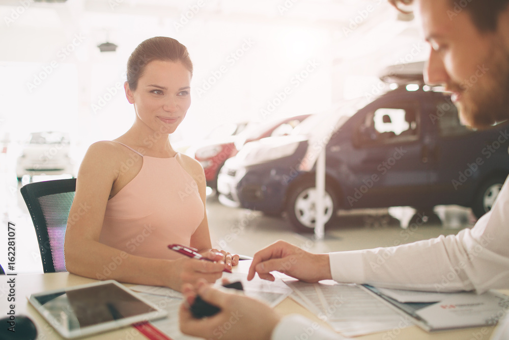 friendly car salesman talking to a young woman and showing a new car inside showroom Signing of contract. friendly car salesman talking to a young woman and showing a new car inside showroom Signing of contract.