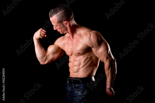 fit muscular man posing isolated on a dark background © verkoka