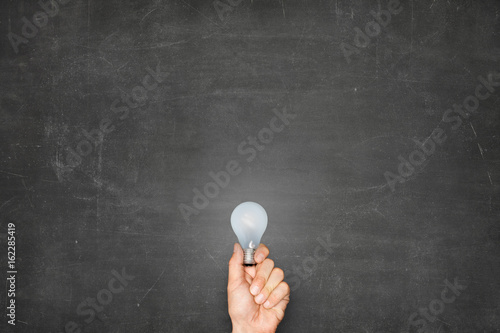 Businessman Holding Light Bulb Against Blank Blackboard