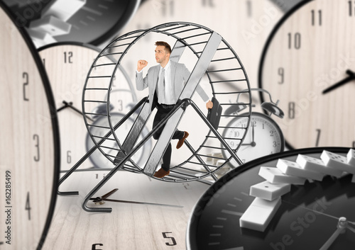 Young man running in wheel and clocks on background. Business rat race concept