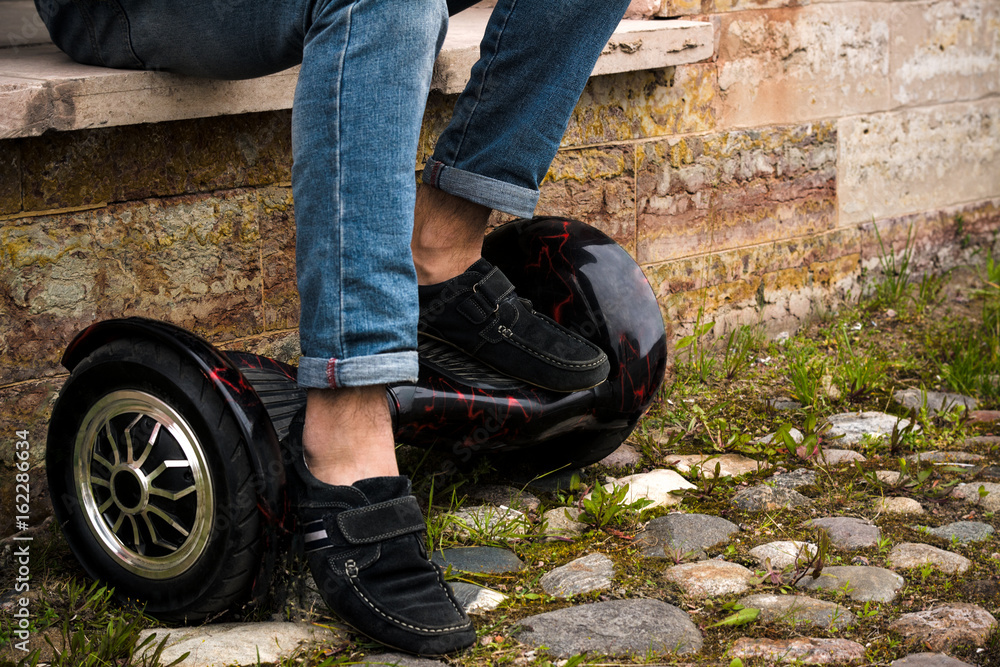 The guy is sitting on the windowsill putting his feet on the hoverboard. The legs of a man dressed in moccasins close-up. The guy is sitting on the windowsill putting his feet on the hoverboard. The legs of a man dressed in moccasins close-up.