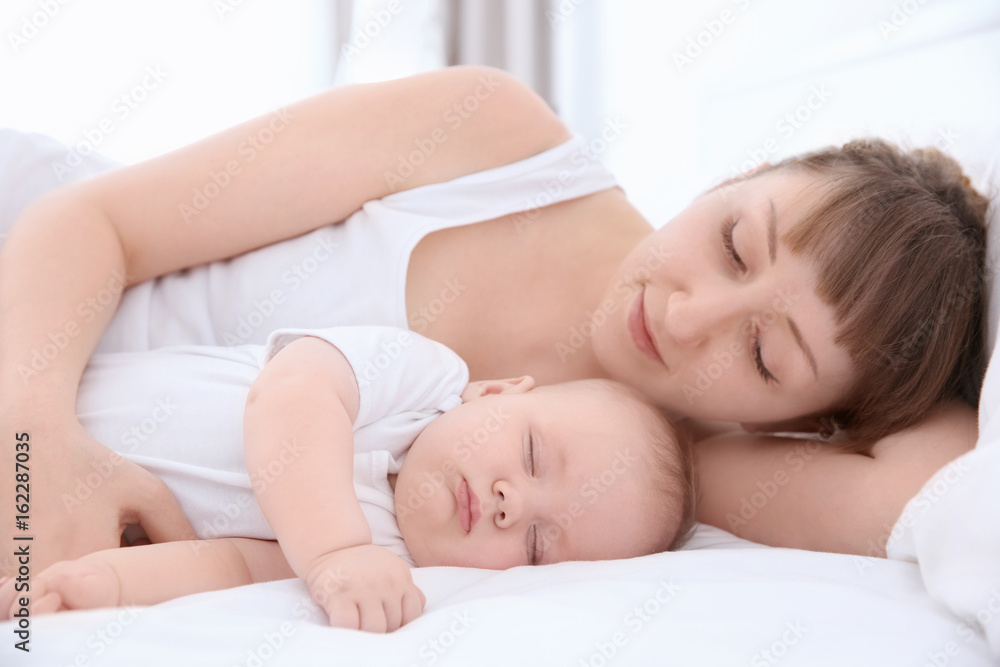 Young woman with cute sleeping baby lying on bed at home Young woman with cute sleeping baby lying on bed at home