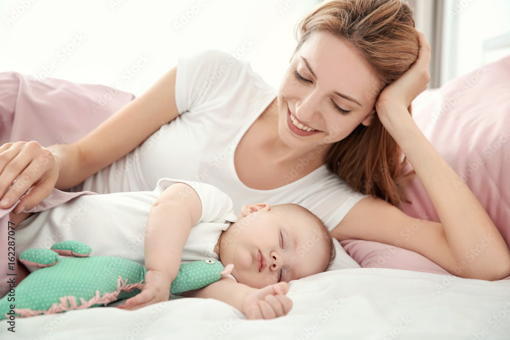 Young woman with cute sleeping baby lying on bed at home Young woman with cute sleeping baby lying on bed at home