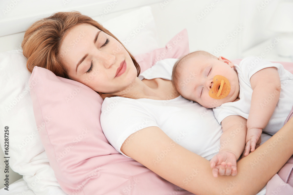 Young woman with cute baby sleeping on bed at home Young woman with cute baby sleeping on bed at home