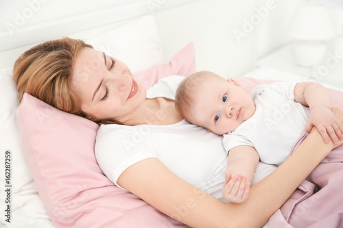 Happy young woman with cute baby lying on bed at home