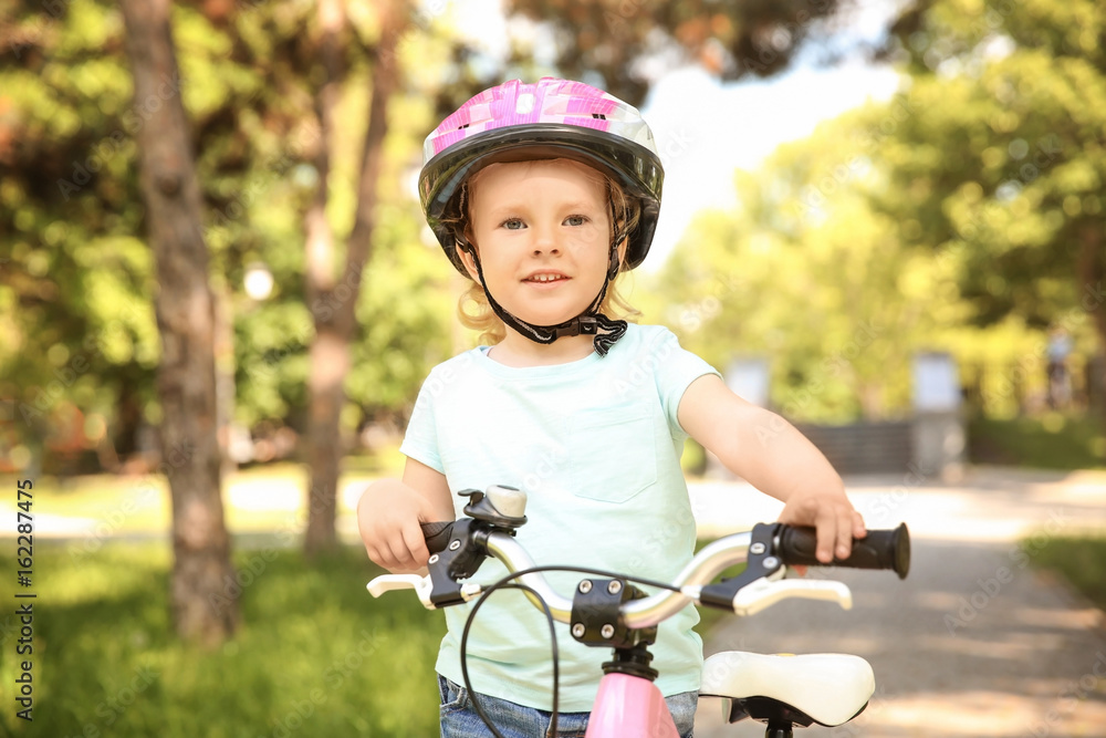 Naklejka premium Cute little girl with bicycle in park on sunny day