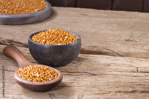 Red millet grains in bowl on wood