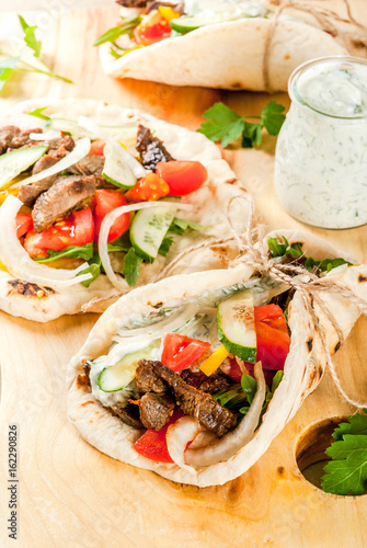 Healthy snack, lunch. Traditional Greek wrapped sandwich gyros - tortillas, bread pita with a filling of vegetables, beef meet and sauce tzatziki. On light stone table Copy space