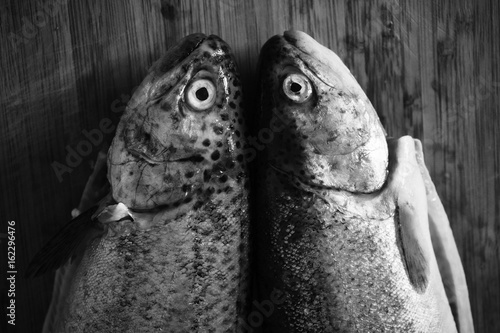 Black and white grunge image of two trout fish prepared to be cooked on a wooden table.