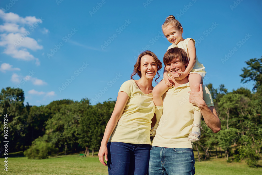 Happy family smiling in the park. Mother, father and daughter in nature on background of blue sky and trees.