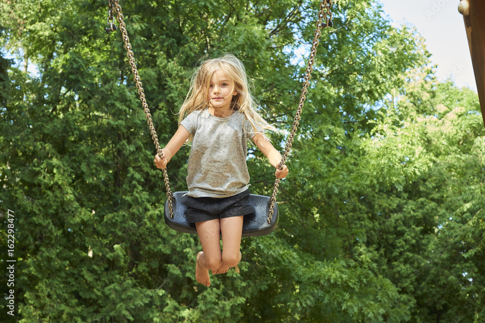Little child blond girl having fun on a swing outdoor. Summer playground. Girl swinging high. Young child on swing outdoors Little child blond girl having fun on a swing outdoor. Summer playground. Girl swinging high. Young child on swing outdoors