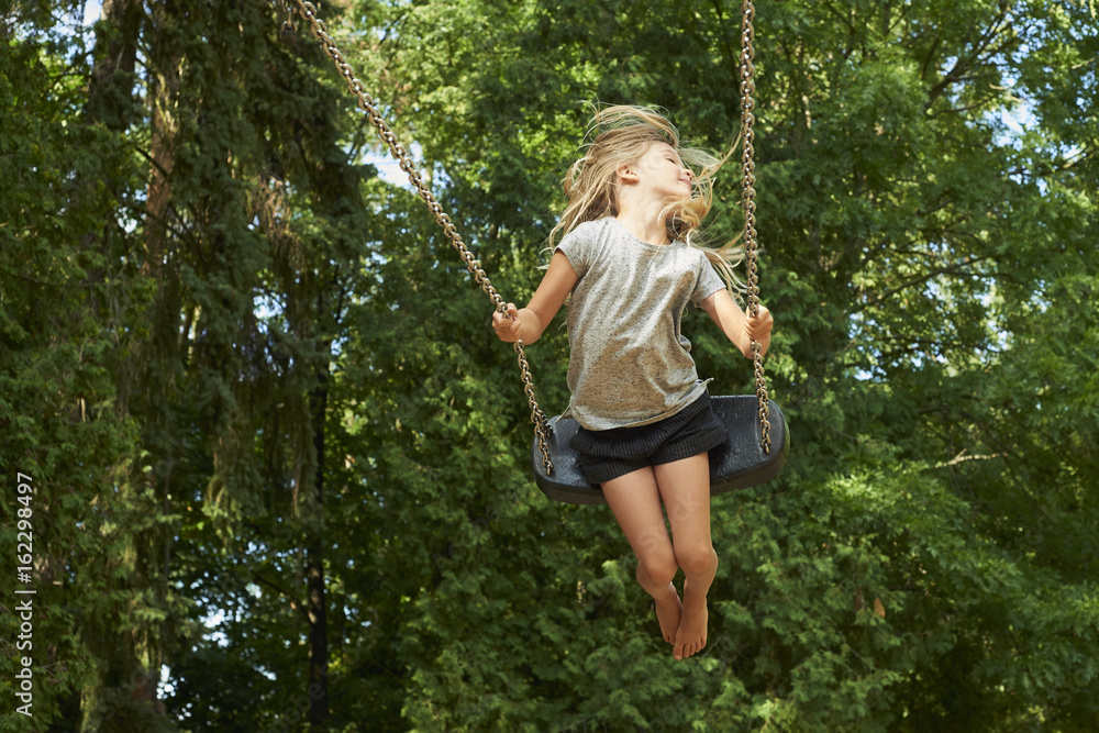 Little child blond girl having fun on a swing outdoor. Summer playground. Girl swinging high. Young child on swing outdoors