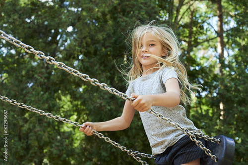 Little child blond girl having fun on a swing outdoor. Summer playground. Girl swinging high. Young child on swing outdoors