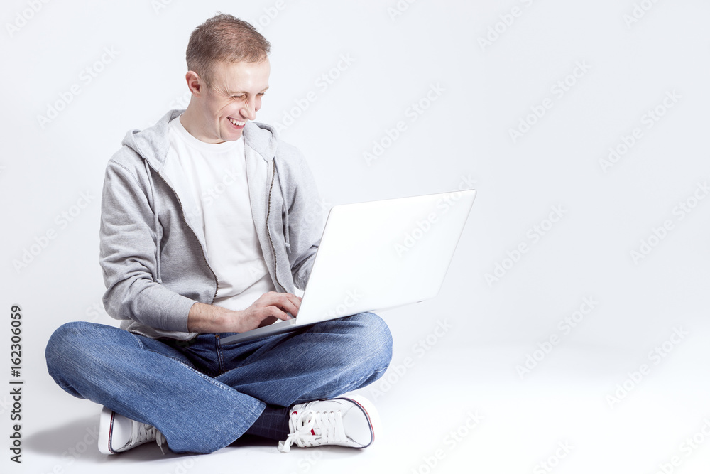 Youth Lifestyle Concepts and Ideas. Portrait of Happy Smiling handsome Caucasian Man Sitting with Laptop on Legs. Posing Against White Background. Youth Lifestyle Concepts and Ideas. Portrait of Happy Smiling handsome Caucasian Man Sitting with Laptop on Legs. Posing Against White Background.