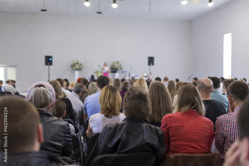 People Sitting In Lines During a Conference While Female Host Speaking on Stage People Sitting In Lines During a Conference While Female Host Speaking on Stage
